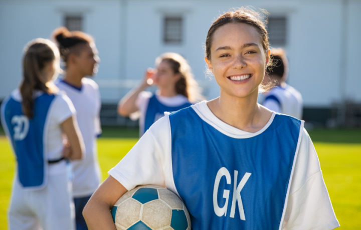 Smiling young athlete holding a soccer ball with her team